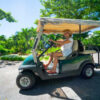 side view happy smiling woman in white dress driving with golf cart in luxury island resort on sunny vacation day